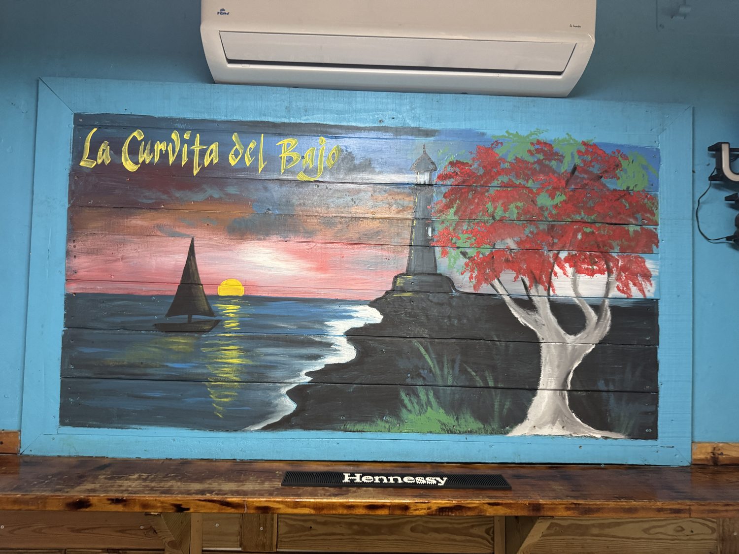 Mural pintado a mano de un atardecer con faro y flamboyán